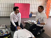 Zwei Rettungsdienstmitarbeiter zeigen, wie die Versorgung eines verletzten Menschen bei einem Verkehrsunfall abläuft.