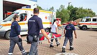 Vier Einsatzkräfte tragen eine Klapptrage mit Gewichten