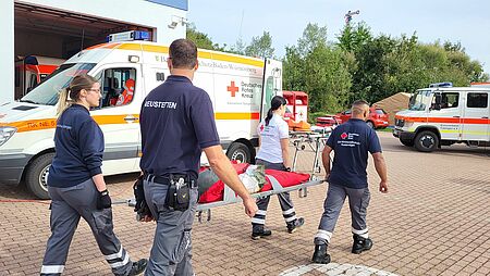 Vier Einsatzkräfte tragen eine Klapptrage mit Gewichten
