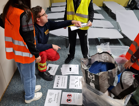 Eine Einsatzkraft der DLRG erklärt Kindern in Warnwesten, wie eine Notunterkunft einzurichten ist