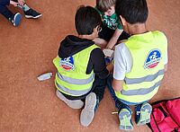 Zwei Kinder in Warnwesten helfen einem verletzten Kind