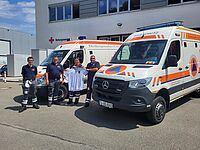 Einsatzkräfte des Sanitätsdienstes stehen mit einem Fußballtrikot vor Einsatzfahrzeugen