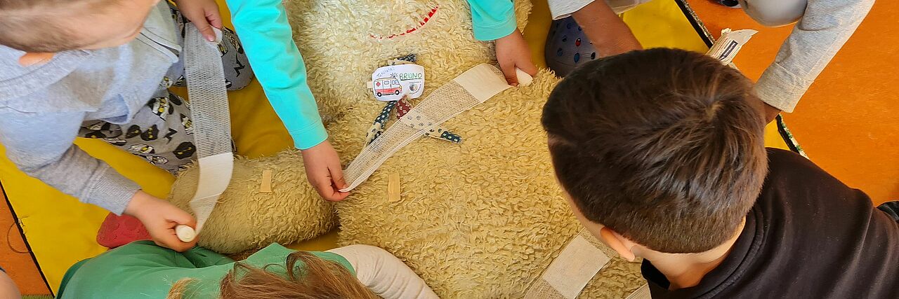 Kindergarten Mini-EH-Kurs Kinder legen einem großen Teddy Verbände an