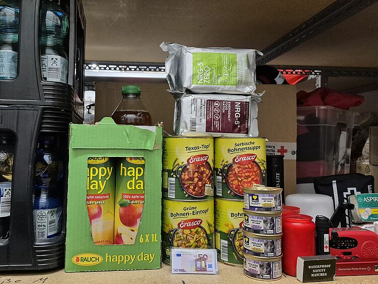 Katastrophenvorsorge Notvorrat Man sieht ein Regalbrett, das mit Getränken, Lebensmitteln, Medikamenten und anderen Hilfsmitteln für eine Katastrophe ausgestattet ist.